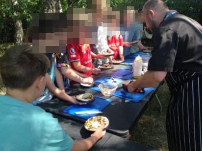 Children preparing food at an outdoor table with a chef